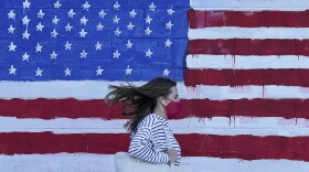 A woman wears a mask while walking past a U.S. flag painted on a wall during the pandemic in San Francisco on Nov. 16, 2020. (Jeff Chiu/AP)