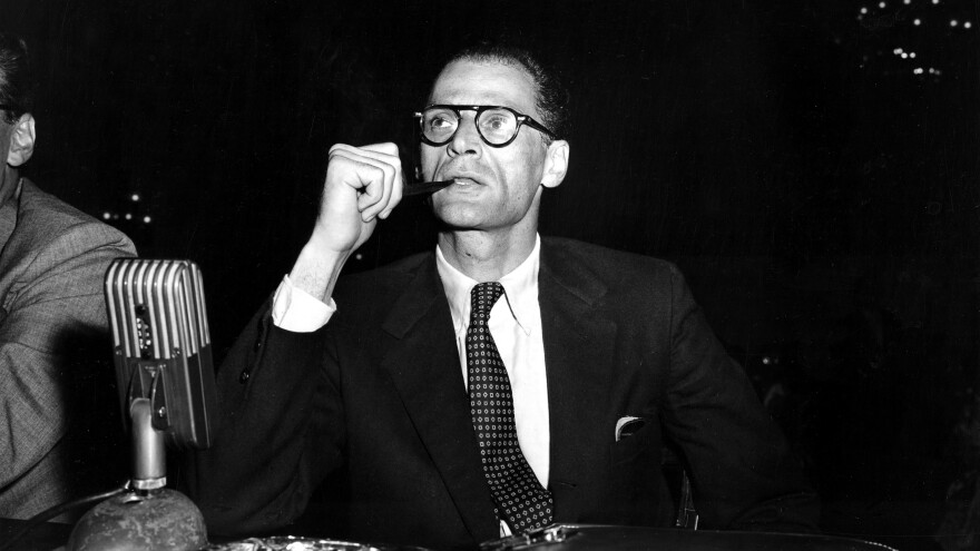 Arthur Miller smokes his pipe at the witness table prior to testifying at a hearing before the House Un-American Activities Committee in Washington, D.C., on June 21, 1956.