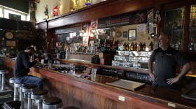 A man sits and eats at a bar as a bartender stands behind it. 