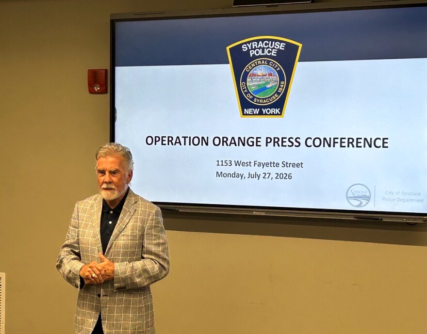 John Walsh speaks in front of a screen that says "OPERATION ORANGE PRESS CONFERENCE"