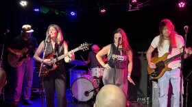 Roasli band performing on stage with a backup singer guitarist bass player and drum kit.