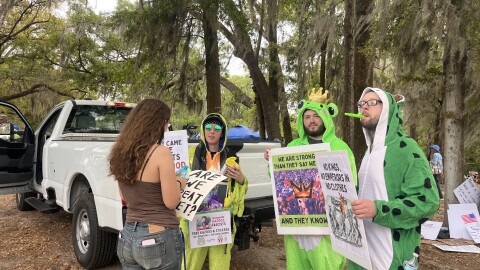 Danielle Patch, Bradley Dees and Kevin Dees, who call themselves “Frogs against Fascism,” were among the estimated thousands of “No Kings” protesters who gathered at Cora P. Roberson Park in Gainesville on Saturday, March 28, 2026. (Sam Gold/WUFT News)