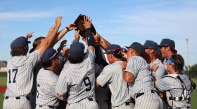 Heartland Community College baseball players in pinstripe uniforms huddle together and raise their hands to the plaque given to the team after winning the NJCAA Division II Central District Championship Tournament on Saturday in Union, Mo.