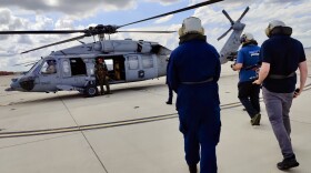 Reporters walking toward a U.S. Navy helicopter. 