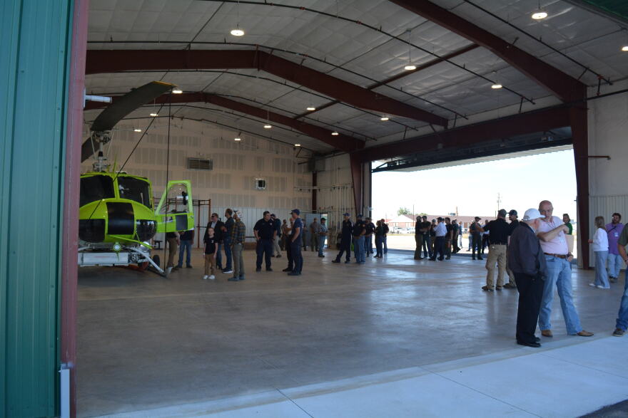 Several groups of people talk inside of a hangar with a bright green helicopter inside.