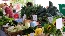 Green Things Farm Collective stand at Saturday's Ann Arbor Farmer's Market. Flowers and vegetables are displayed on a table in front of workers, with customers browsing the stand