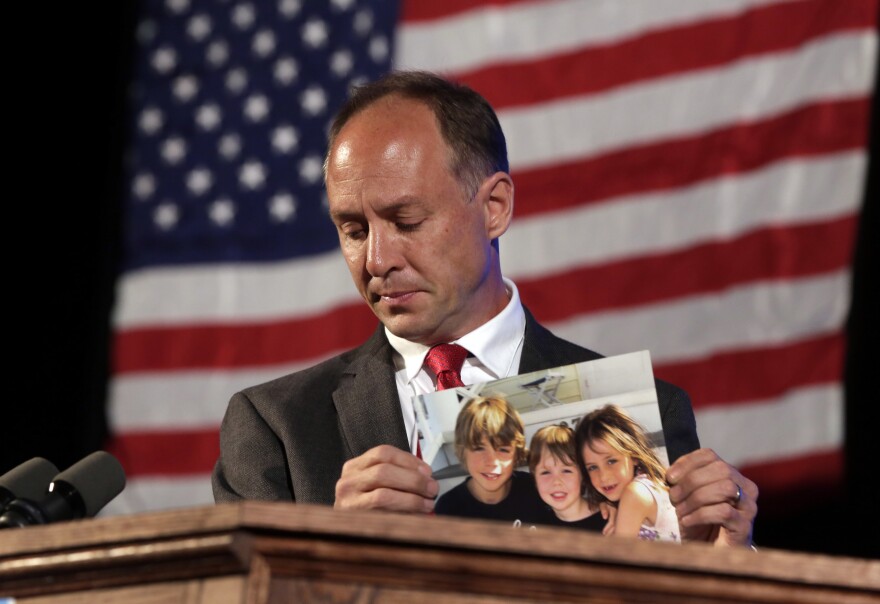 Mark Barden, father of a 7-year-old boy killed at the Sandy Hook Elementary School shooting in Newtown, Conn., holds a photo of his three children during his speech at the state's Democratic Convention, in Melville, N.Y., in 2014. Barden is one of 10 plaintiffs suing Remington Arms Co., the manufacturer of the assault rifle used in the mass murder.