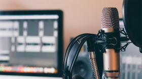 A grey microphone with headphones hung on it in front of a blurry background.