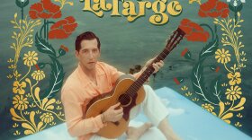 Album cover for Pokey LaFarge's 2024 album "Rhumba Country." Pokey is sitting on a white platform with water behind him. He is holding an acoustic guitar there are flowers overlaid on the photo around him. 