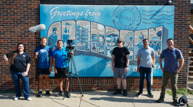 The Dakota Life team in front of a Greetings from Aberdeen mural
