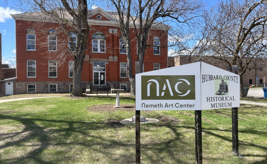 A sign in front of an old brick building surrounded by trees and green grass.