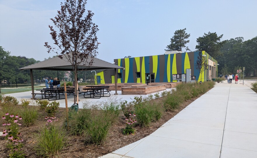 A photo taken outside shows people sitting outside and a yellow, green and brown striped building.