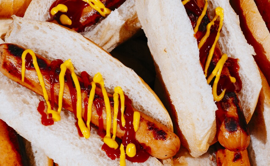 A pile of hot dogs in buns with ketchup and mustard