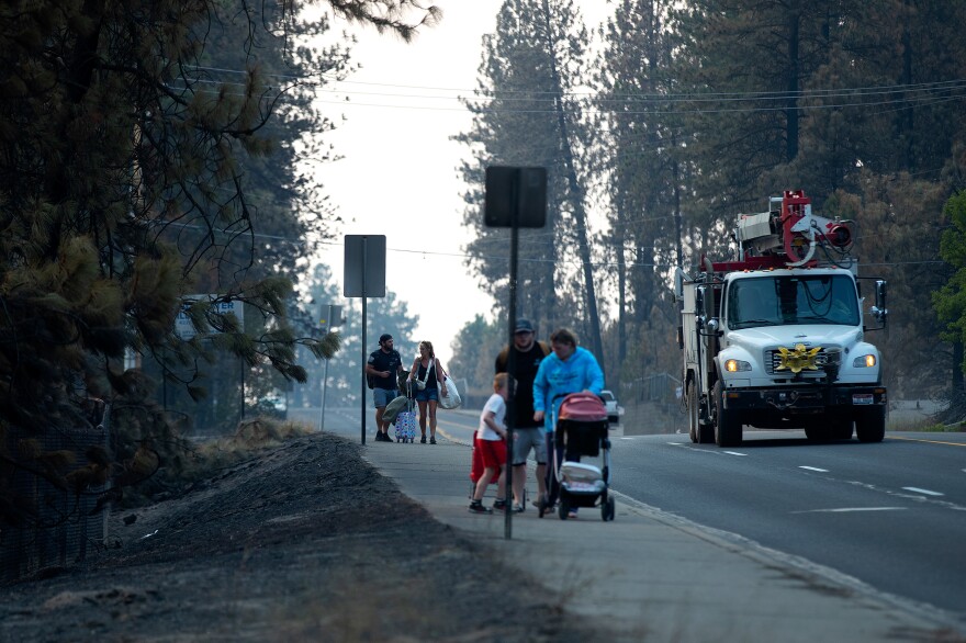 Evacuees walk along North Indian Trail Road carrying their belongings as the Old Trails fire continues to burn on Wednesday, August 5, 2026, in northwest Spokane. Vehicles were not able to cross the barricade and residents transported each other and their belongings with the vehicles that remained inside the perimeter.