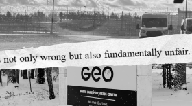 A black-and-white collage with three horizontal layers. The top image features a high-security fence with razor wire and a transport van. A jagged, torn-paper strip is overlaid across the center with the text: "not only wrong but also fundamentally unfair." The bottom image is a sign for the "GEO North Lake Processing Center" located at 1805 West 32nd Street. The sign and surrounding ground are covered in a layer of snow, with trees visible in the background.