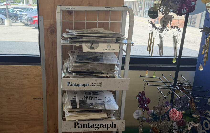 An in-store newsstand with stacks of out-of-date newspapers placed inside of a window.