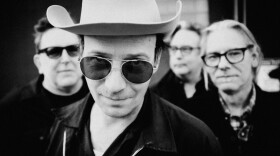  A black and white photo of Erik Koskinen with his band behind him. He is wearing dark sunglasses and a cowboy hat.