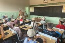 Children listening to a teacher in a old fashioned one-room school house