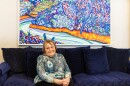 Marlene Gregor sitting in her home with an original Harold Gregor painting behind her.