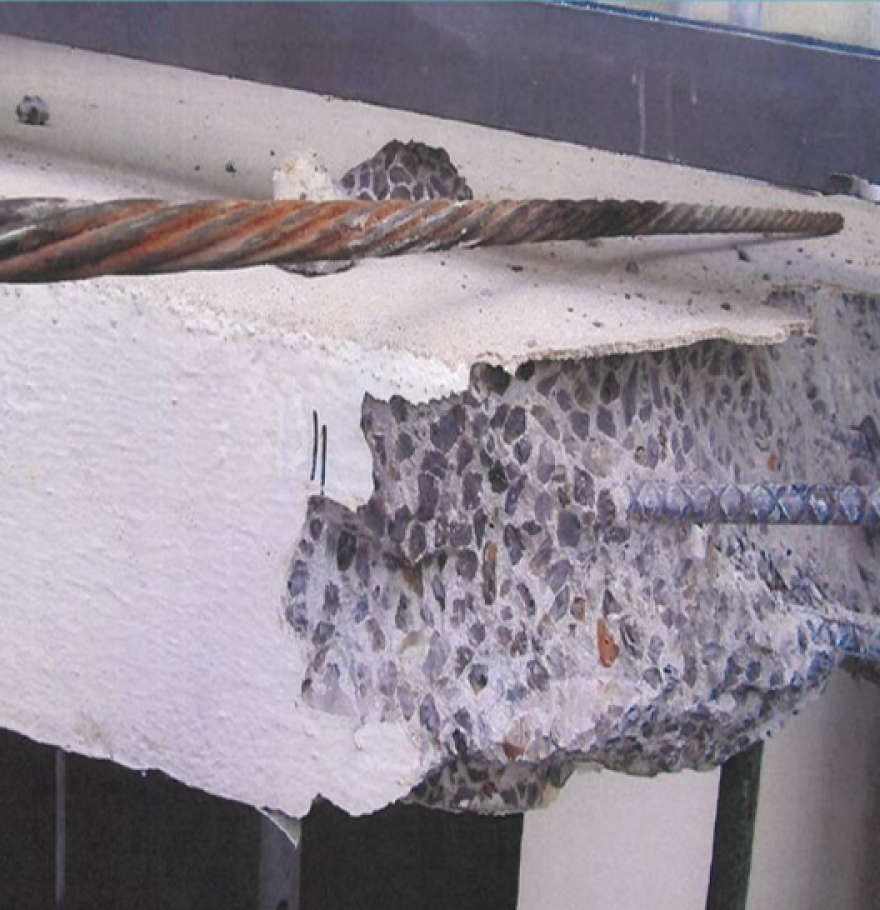 A close-up on corrosion of a structural element to a condo building. Sections of concrete have broken away, reveling metal bars.