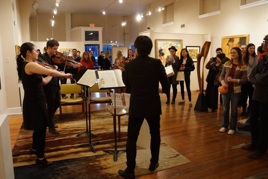color photograph of two violiists and a violist standing up in an art gallery and playing their instruments