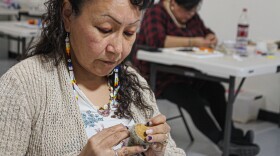 An Alaska Native woman stitches some pieces of leather