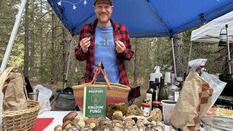 Dr. Gordon Walker poses behind a table of mushrooms and his book “Passport to Kingdom Fungi.”