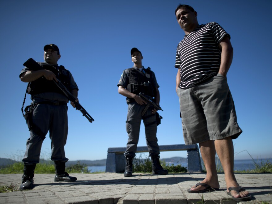 Alexandre Anderson, president of a fishermen's association, stands near Guanabara Bay, guarded by two policemen, in 2012. He is under federal protection for his role in supporting the fishermen. Fellow fishermen have been killed or have disappeared. He says they have been targeted for opposing industrial projects that pollute the bay.
