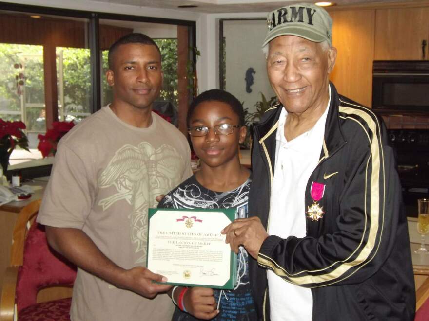 Walter Morris, Michael Fowles, and Morris' great grandson Justice Fowles holding up a Legion of Merit Award.