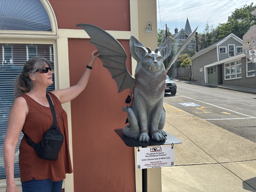 Christie Hicks pointing out details added by artists on "Purrgoyle Protector- The Whiskered Watcher by artist Dionne Gule and Mikal Gule. This cat is sponsored by William Street Experiences.