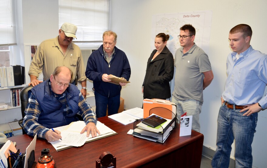 Delta County Emergency Management Coordinator Monty Hobbs (seated) signs paperwork with Commissioner Gary Anderson. Also present was Mark Brewer, Lindsay Kempner, Barron McLeod, and Tanner Crutcher. 