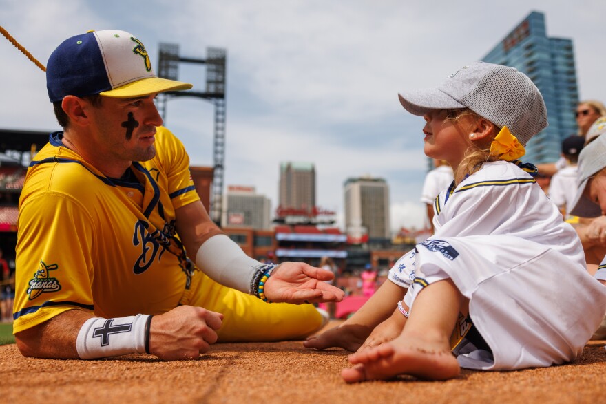David Meadows, left, and young Banana fan Reign Moore, right, play in the dirt on the field together ahead of the game between the Savannah Bananas and the Party Animals at Busch Stadium on Friday, July 18, 2025, in downtown St. Louis. Moore and her family were acknowledged on the field ahead of the game as the Banana Foster family of the game.