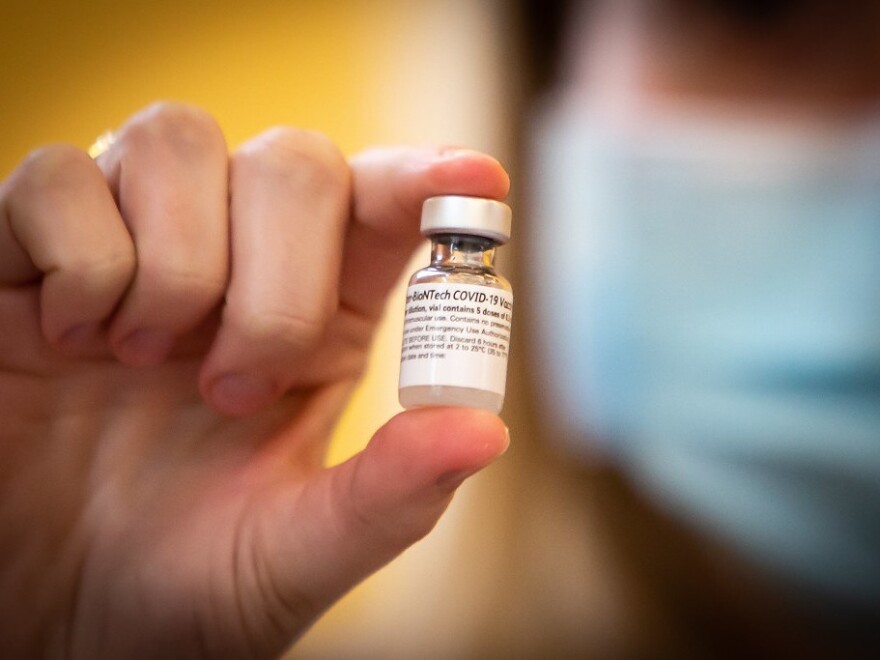 A person's hand holds a vial of the COVID vaccine. 