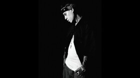 A man in a black-and-white photo looks at the ground while standing against a black background.