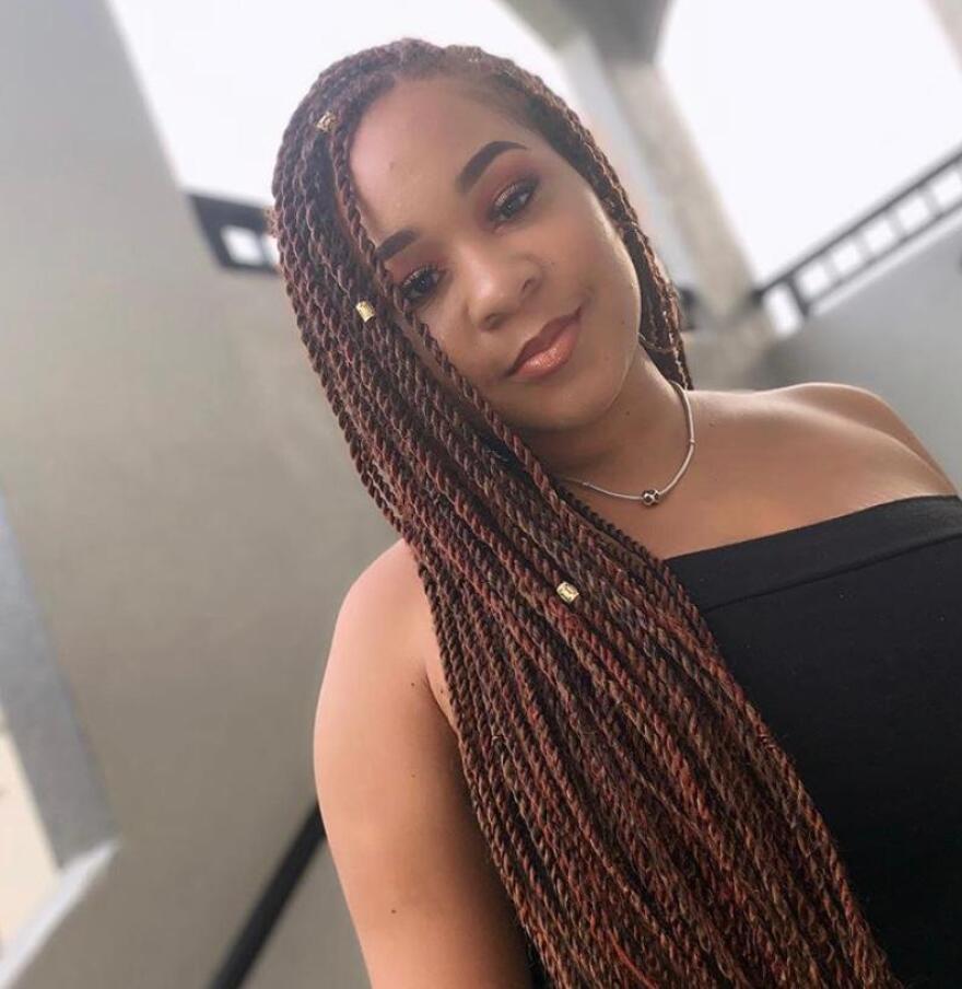 A woman with long braids smiles for a camera.