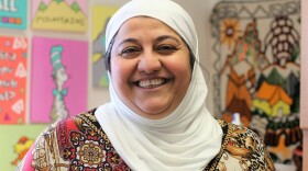 A woman wearing a white head scarf smiles at the camera.