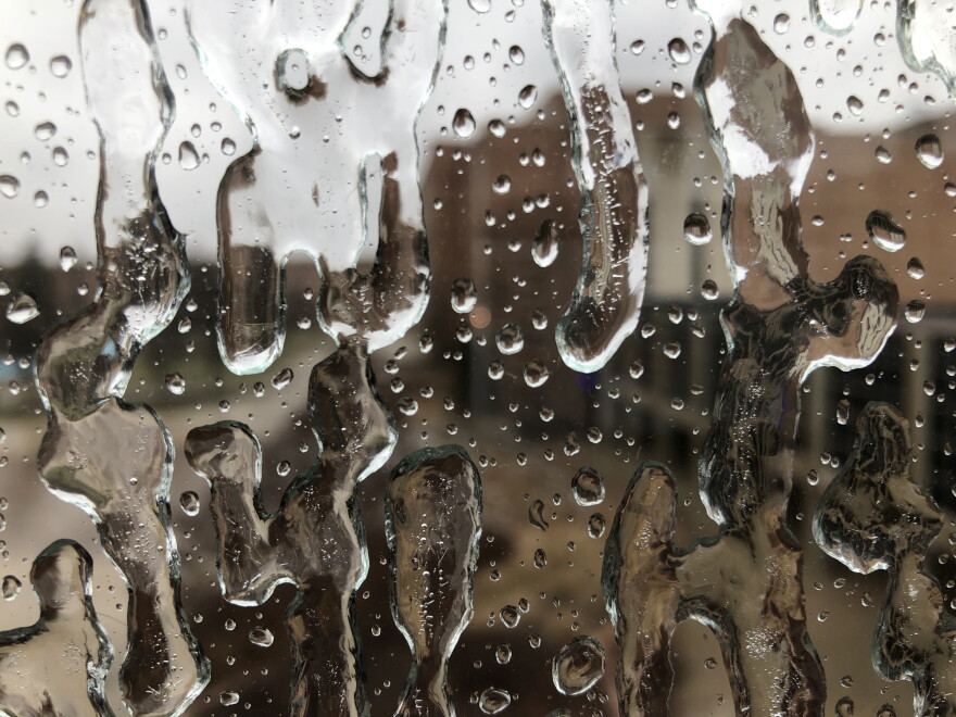 Close up view of ice and water on a glass window, with blurred view of buildings in the background