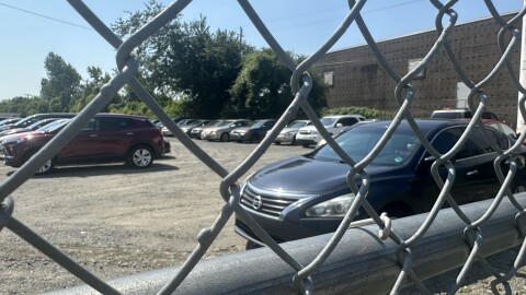Cars sit behind a chain-link fence in a tow lot.