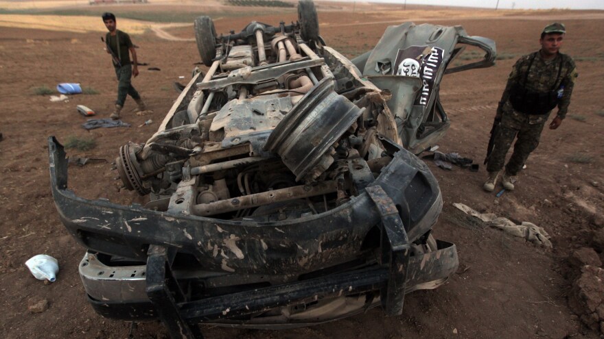 Peshmerga fighters inspect the remains of a car bearing an image of the trademark jihadist flag, after it was targeted by an American airstrike in the village of Baqouba, north of Mosul. The car reportedly belonged to Islamic State militants