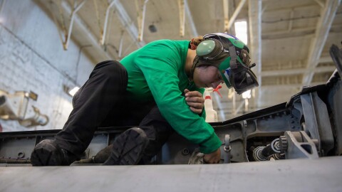 A sailor cleans the wing of an F/A-18F Super Hornet aircraft in the hangar bay of the USS Gerald R. Ford (CVN 78) during Operation Epic Fury.