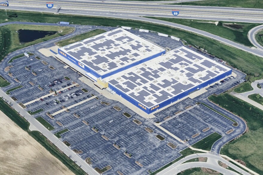 A Google Earth screenshot shows an aerial view of the Ikea in Fishers. The roof of the massive building is littered with neat, geometric clusters of solar panels. The building is painted blue with "IKEA" written in yellow font at its corners. In the 