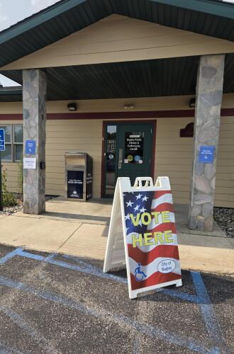 A "Vote Here" sign featuring the American flag directs Bagley voters where to cast ballots on Primary Election Day, Aug. 11, 2026, at the Bagley Public Library.