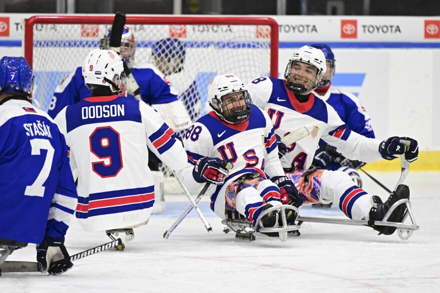 Kevin McKee wears a team USA jersey and is surrounded by other sled hockey players on the ice. 