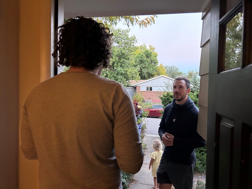 Two men stand in a doorway and talk with each other.