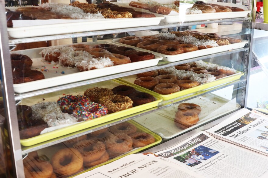 Local and national newspapers for sale in front of Washtenaw Dairy's doughnut display.