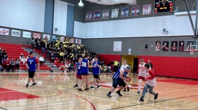 High schoolers play basketball with a band in the background. 