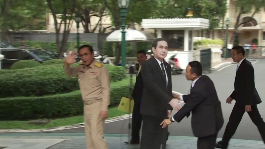 In this image from video, Thailand's Prime Minister Prayuth Chan-ocha (left) waves and walks off as a life-sized cardboard cut-out figure of himself is placed next to the microphone during a media conference in Bangkok on Monday.