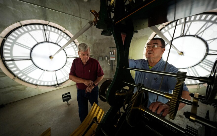Two people work on gears for a massive clock