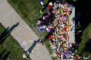 An aerial view of a memorial of flowers, balloons, and sidewalk chalk near a grassy area.