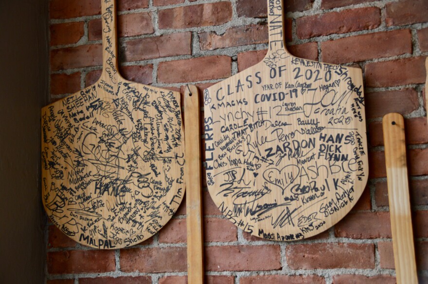 Pizza paddles with marker writing on them hang on a brick wall